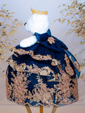 White teddy bear wearing a navy blue embroidered outfit with gold details and a crown.